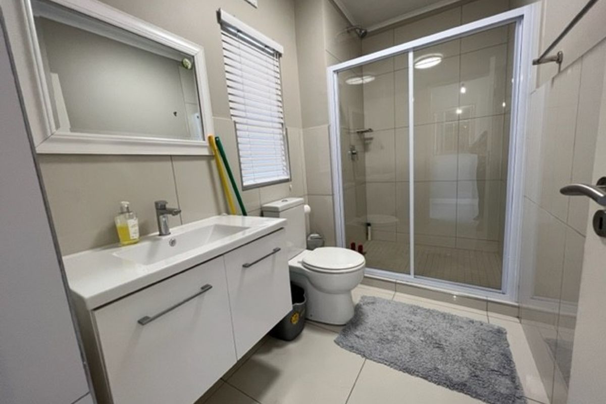 A modern bathroom featuring a white vanity with integrated basin, a glass-enclosed shower, and neutral wall and floor tiling.