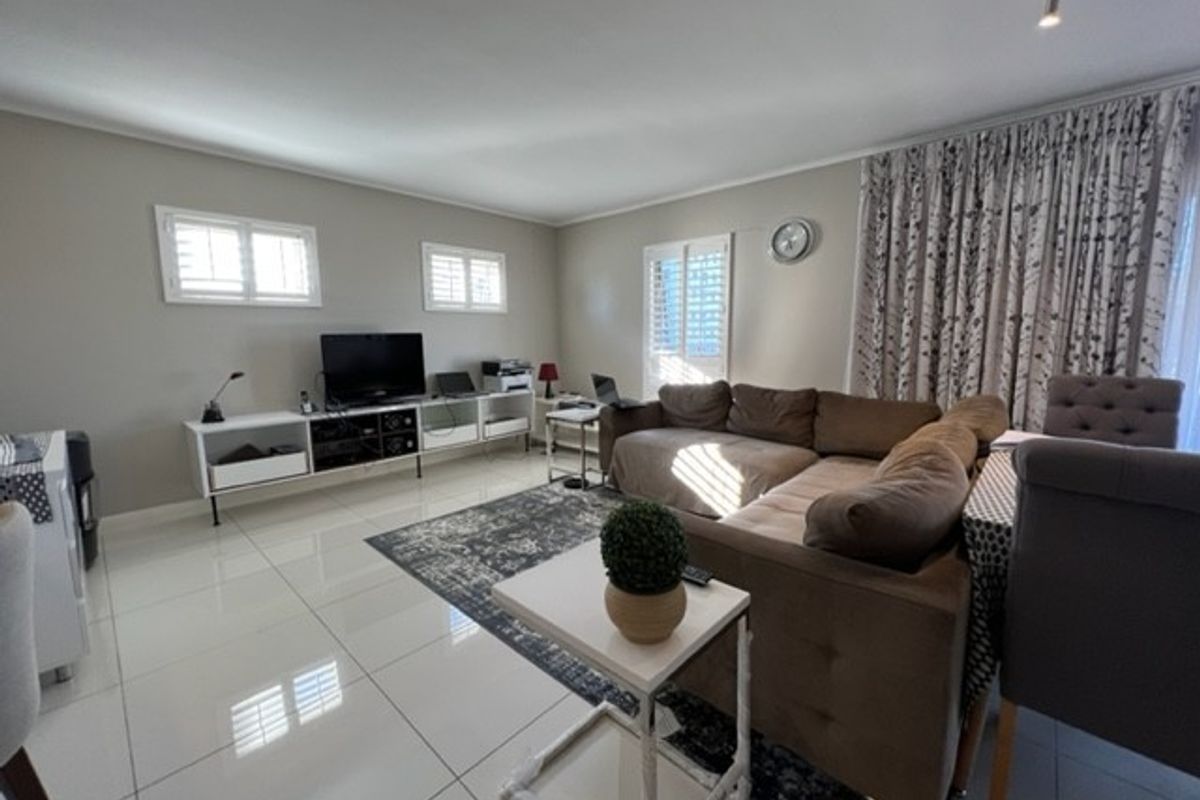 A bright and spacious living area featuring large format floor tiles, plantation shutters, and neutral wall finishes.