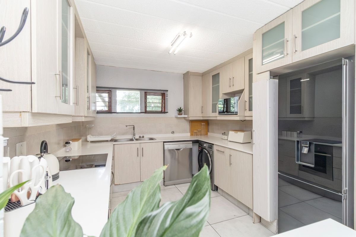 A functional kitchen featuring light wood-finish cabinetry, ample counter space, tiled flooring, and integrated appliances including a dishwasher and built-in microwave.