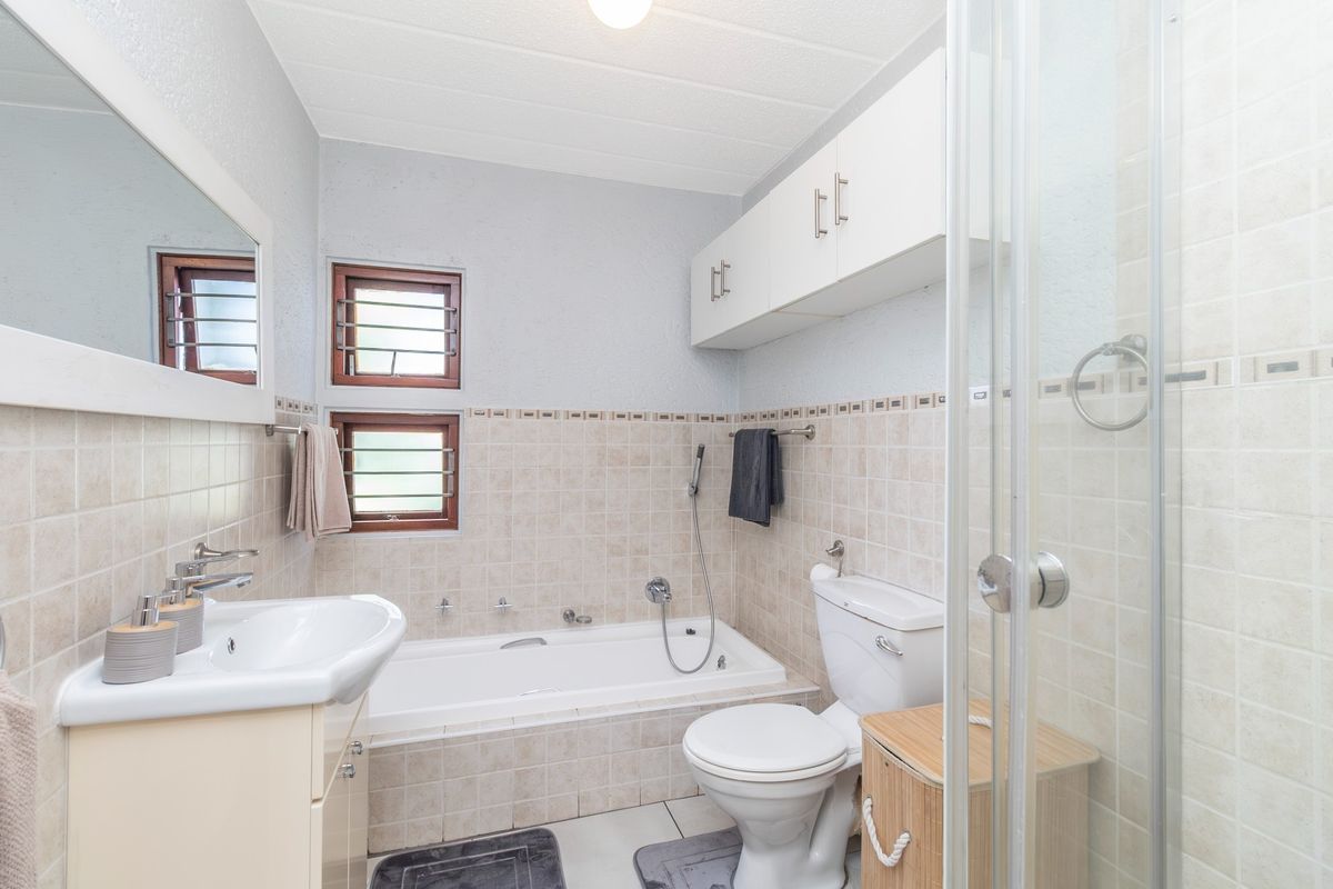 A functional bathroom featuring a built-in bathtub, separate shower enclosure, vanity unit, and wall-mounted storage cabinetry with neutral tiled finishes.