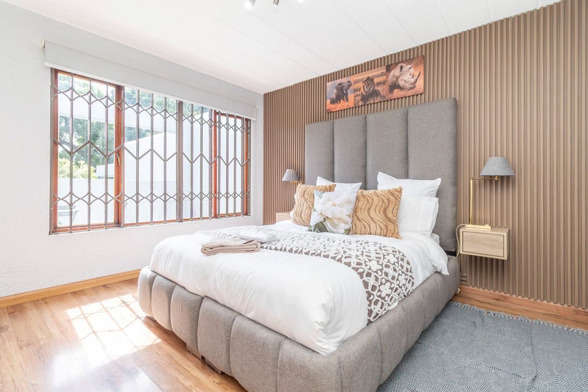 A well-maintained bedroom featuring timber flooring, a modern vertical slat feature wall, and a window fitted with a security gate.