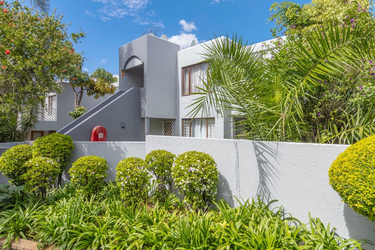 Exterior view of a modern apartment complex featuring a concrete boundary wall, landscaped garden, and external staircase access.