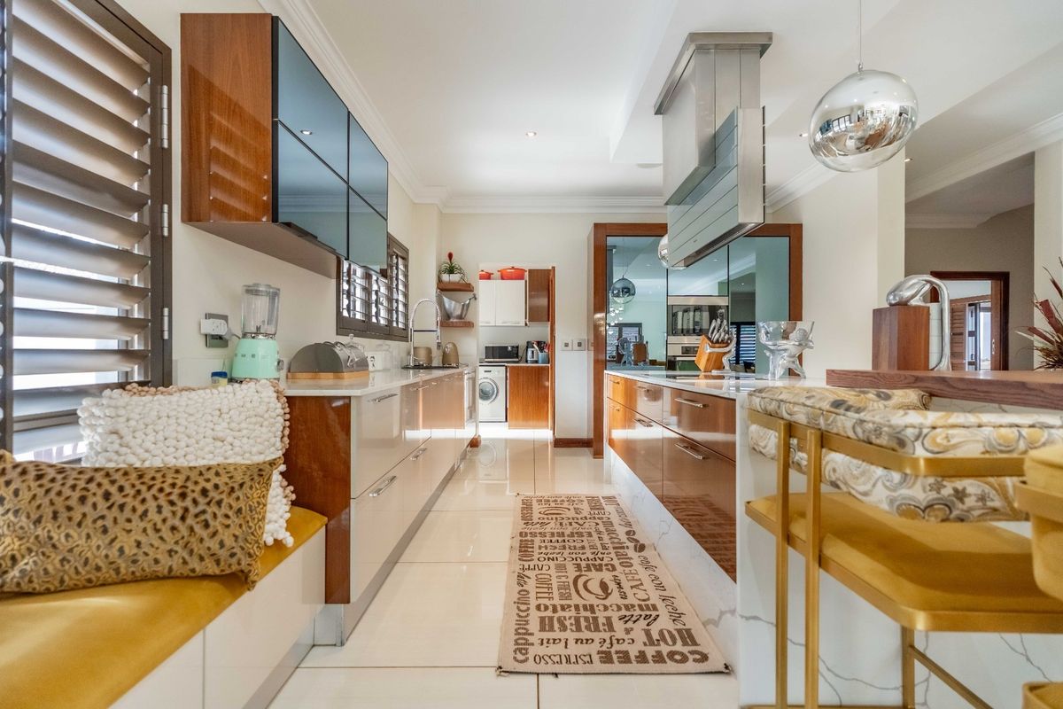 Modern kitchen featuring high-gloss cabinetry, stone countertops, a stainless steel extractor fan, and a built-in breakfast nook with tiled flooring.