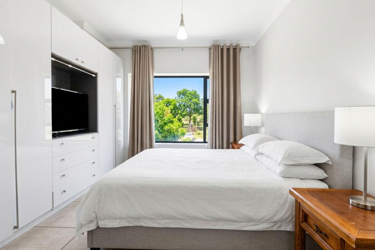 A well-lit bedroom featuring extensive built-in white cabinetry with integrated shelving and a large window offering a pleasant green outlook.
