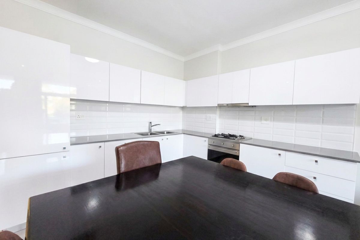 Modern kitchen featuring white high-gloss cabinetry, subway tile backsplash, integrated oven, gas hob, extractor fan, and stainless steel sink.