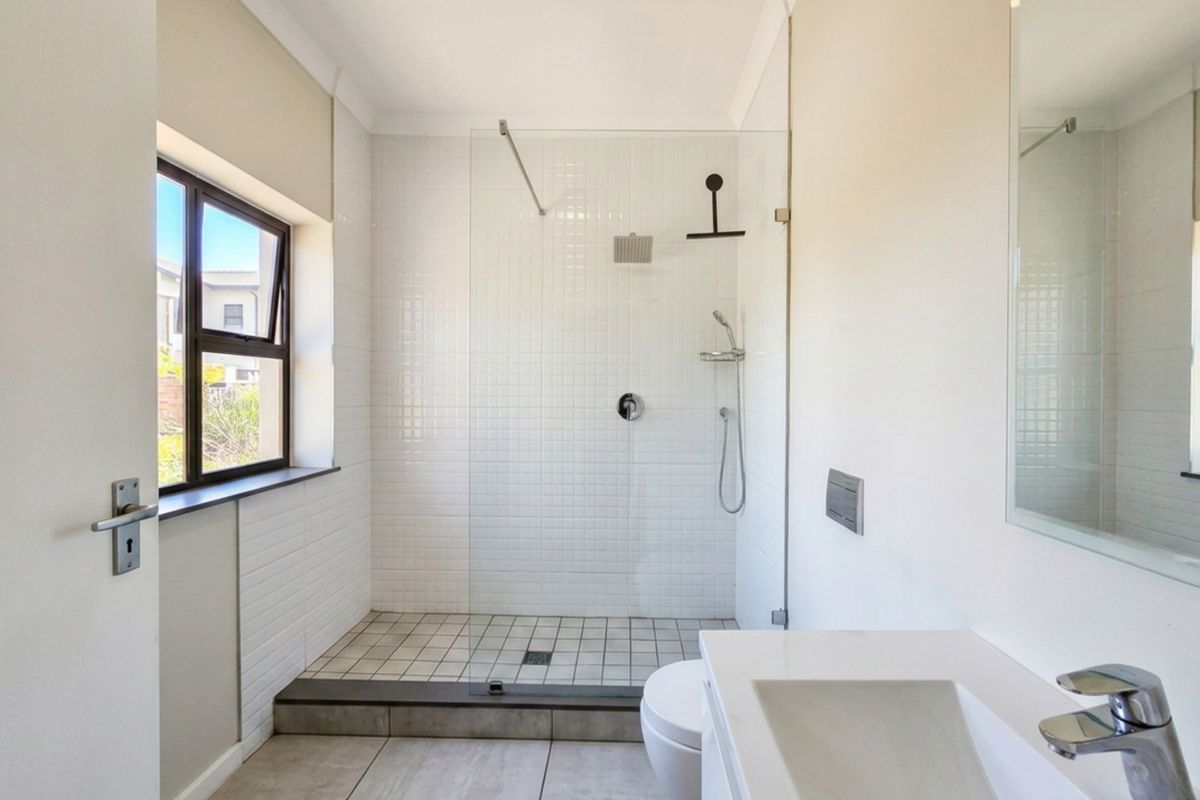 A modern bathroom featuring a walk-in shower with glass screen, wall-mounted vanity, and neutral tiling throughout.