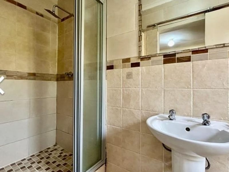 A functional bathroom featuring a tiled shower enclosure with a glass door and a classic pedestal basin with a wall-mounted mirror.