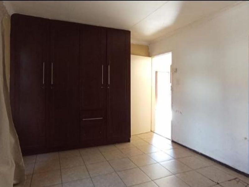A bedroom featuring built-in dark wood cabinetry and tiled flooring, offering a functional space with direct access to an adjacent area.