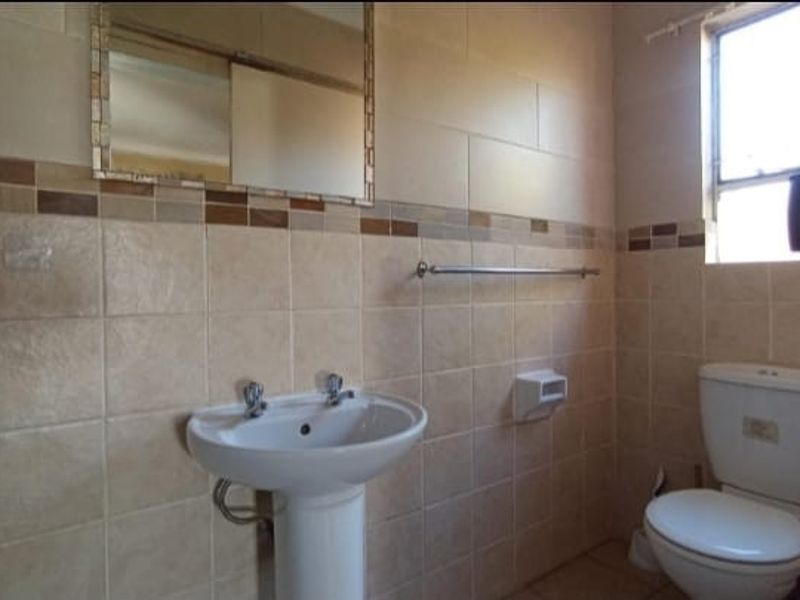 A functional bathroom featuring a pedestal basin, wall-mounted mirror, and a standard toilet with tiled walls and flooring.