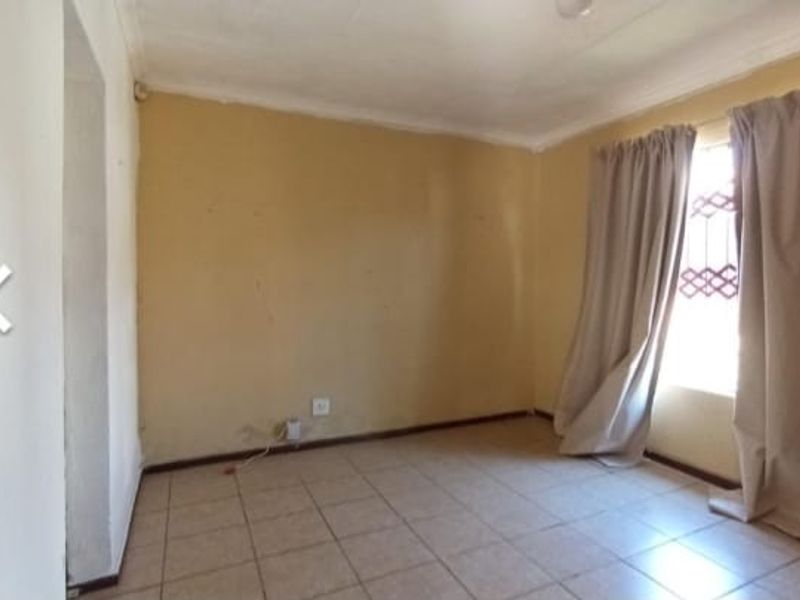 A vacant bedroom featuring tiled flooring, neutral wall paint, and a window fitted with security bars and curtains.