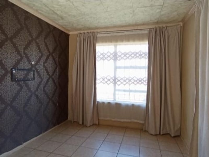 A bedroom featuring tiled flooring, a feature wall with patterned wallpaper, and a window with security bars.