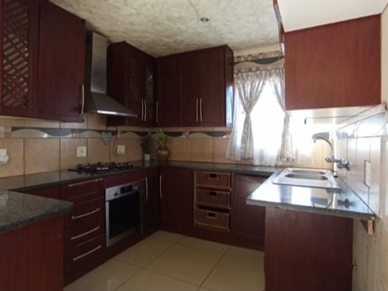 A functional kitchen featuring dark wood cabinetry, granite countertops, a built-in oven, gas hob, stainless steel extractor fan, and a double sink.