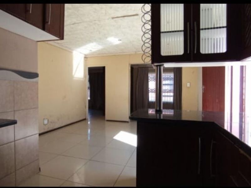 An open plan kitchen and living area featuring tiled flooring, dark cabinetry, and a breakfast counter, requiring cosmetic updates to the walls and ceiling.