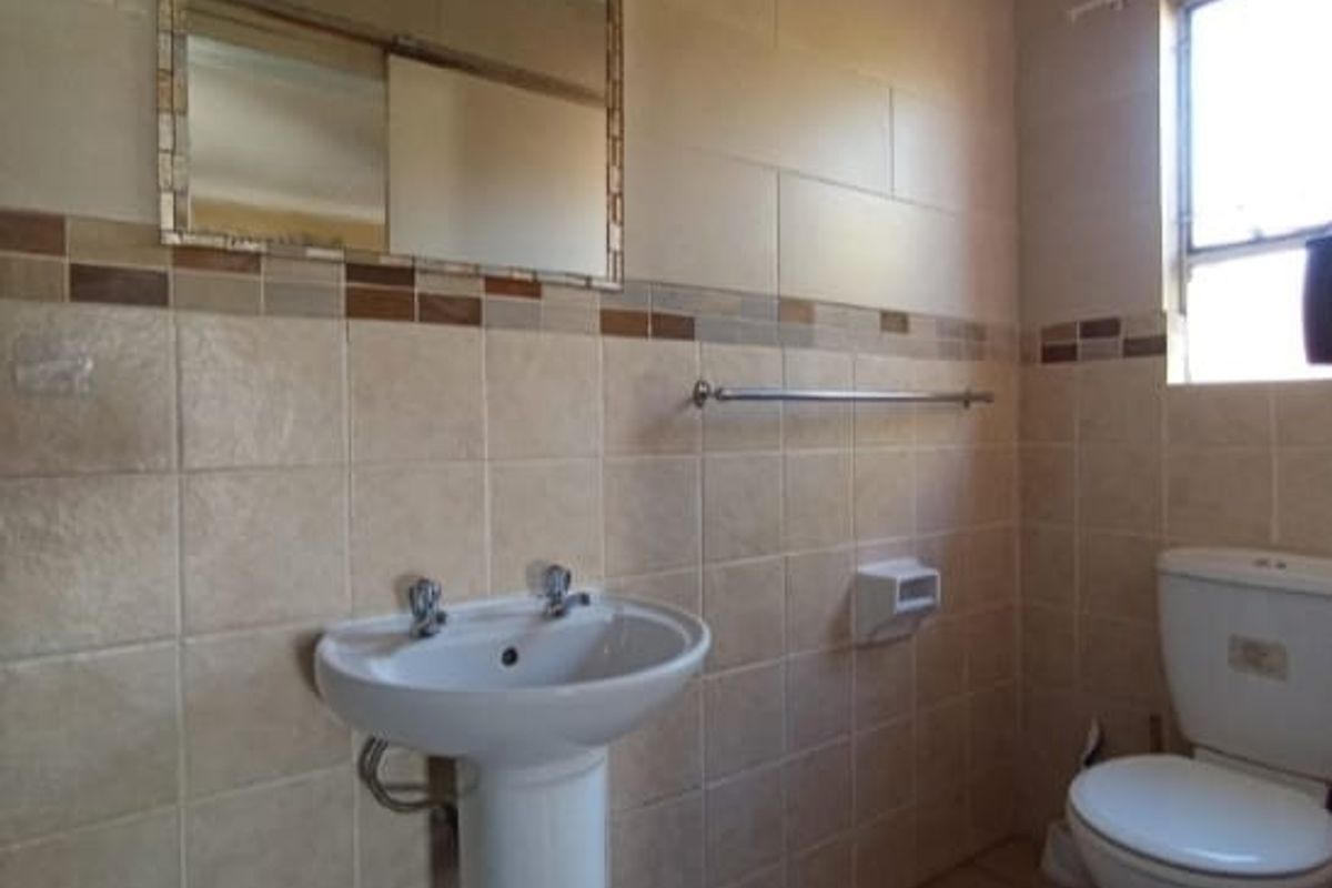 A functional bathroom featuring a pedestal basin, wall-mounted mirror, and a standard toilet with tiled walls and flooring.
