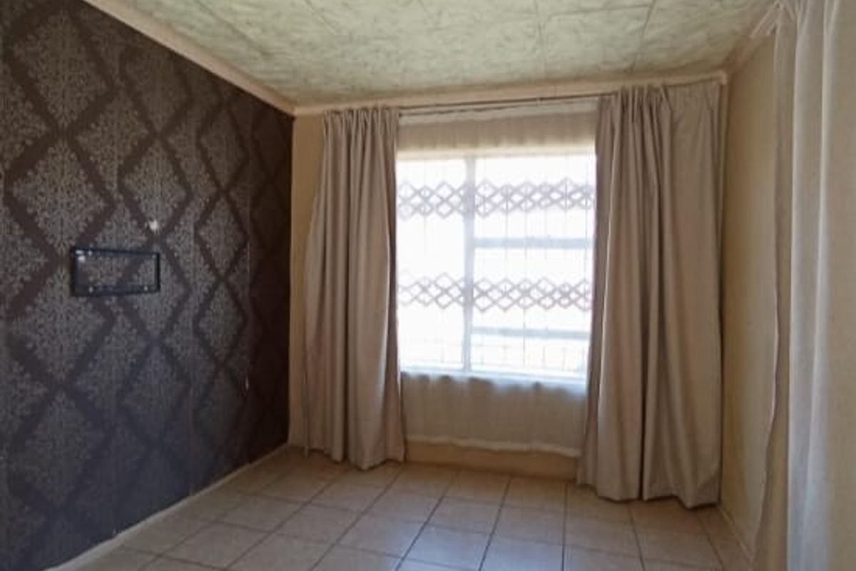 A bedroom featuring tiled flooring, a feature wall with patterned wallpaper, and a window with security bars.