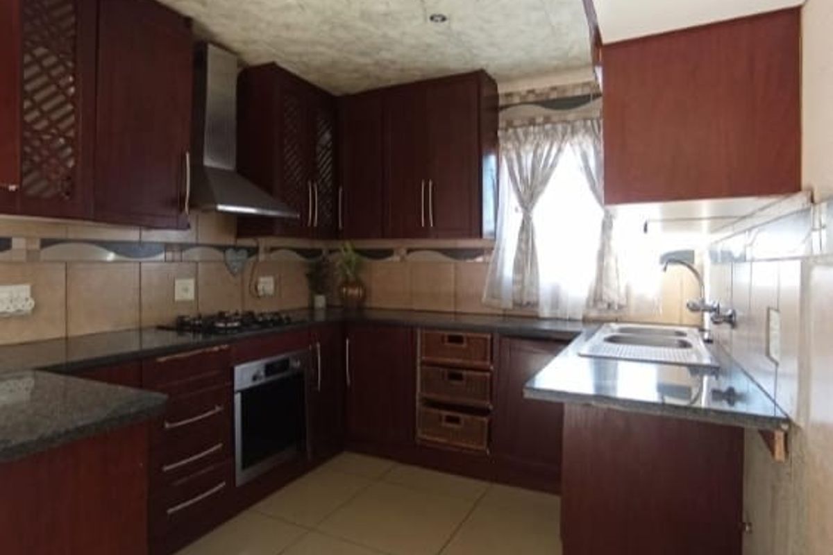 A functional kitchen featuring dark wood cabinetry, granite countertops, a built-in oven, gas hob, stainless steel extractor fan, and a double sink.