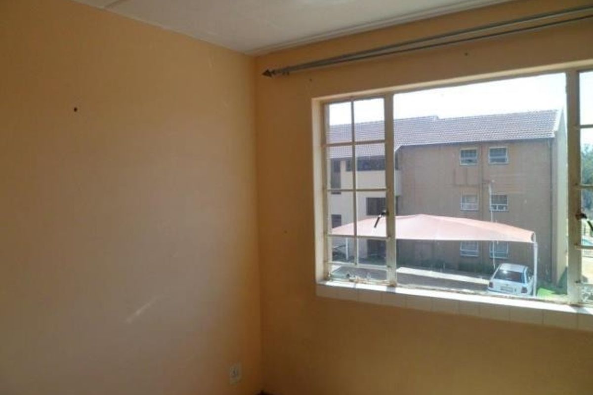An empty bedroom featuring a steel-framed window with a curtain rod, requiring minor cosmetic updates to the wall finishes.