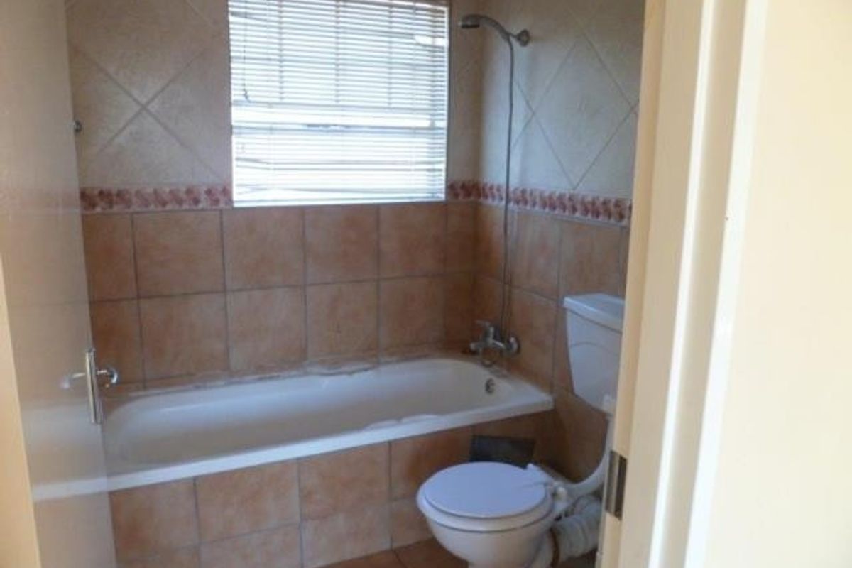 A dated bathroom featuring a bathtub with shower attachment, toilet, and ceramic tiling throughout. The space requires cosmetic updates to modernize the finishes.