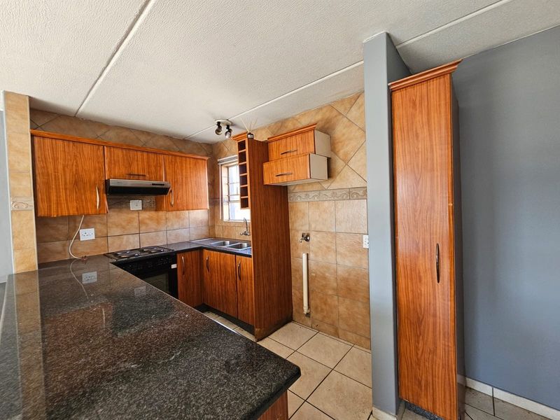 A functional kitchen featuring granite countertops, built-in wooden cabinetry, a built-in oven with extractor fan, and tiled finishes throughout.