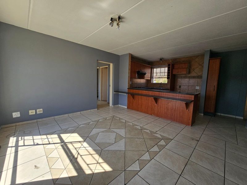 Open-plan living and kitchen area featuring tiled flooring, a breakfast bar, and built-in wooden cabinetry with a tiled backsplash.