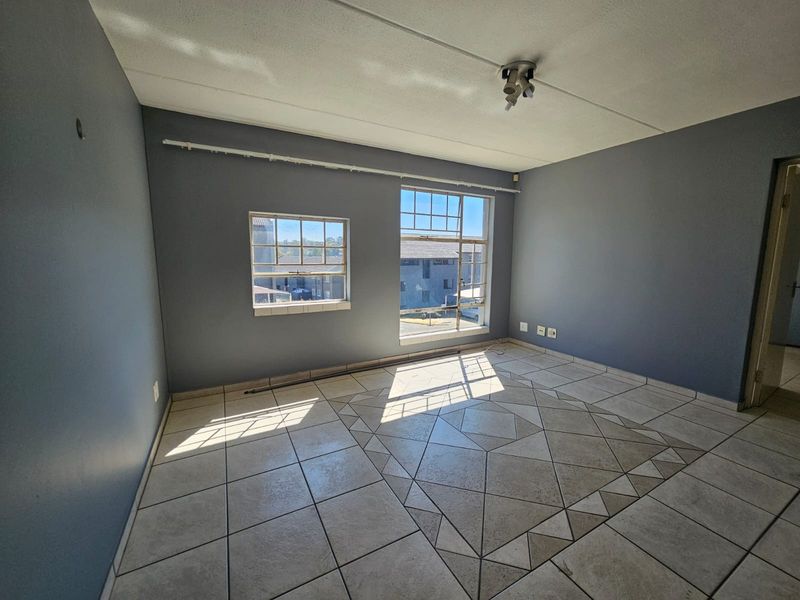 An empty bedroom featuring tiled flooring with a decorative pattern, grey painted walls, and natural light from multi-pane windows.