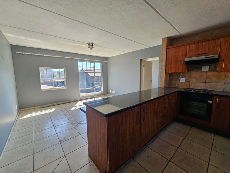 Open-plan kitchen and living area featuring wood-finish cabinetry, granite countertops, built-in oven and hob, and tiled flooring throughout.