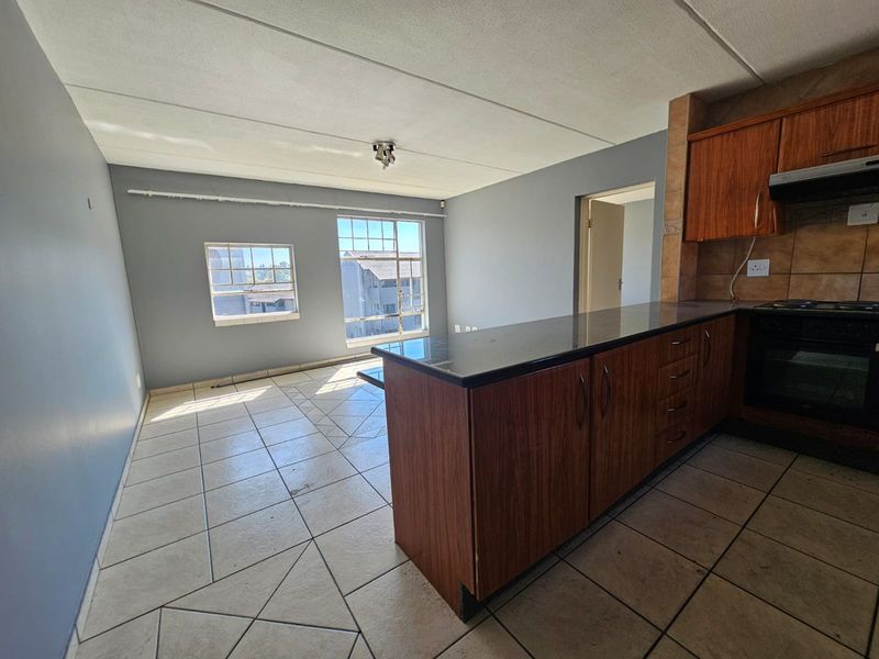 Open-plan living and kitchen area featuring tiled flooring, wooden cabinetry, granite countertops, and built-in cooking appliances in a neutral color scheme.