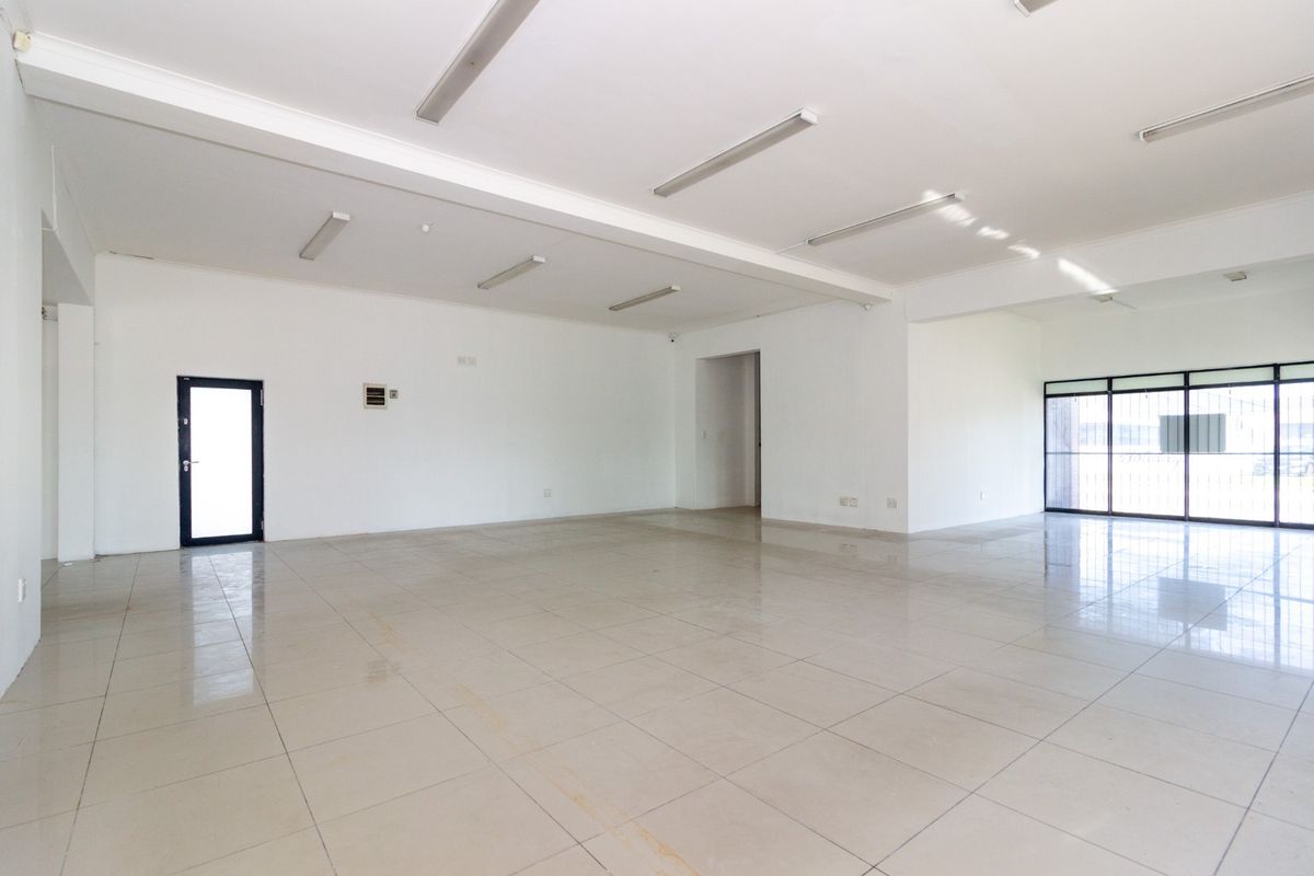 Spacious open-plan retail area featuring neutral tiled flooring, ample natural light from large windows, and functional overhead fluorescent lighting.