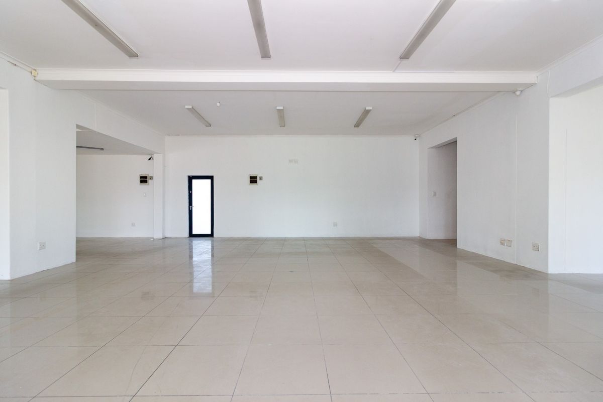 A spacious, vacant open-plan retail area featuring neutral tiled flooring, clean white walls, and overhead fluorescent lighting, suitable for various commercial business layouts.