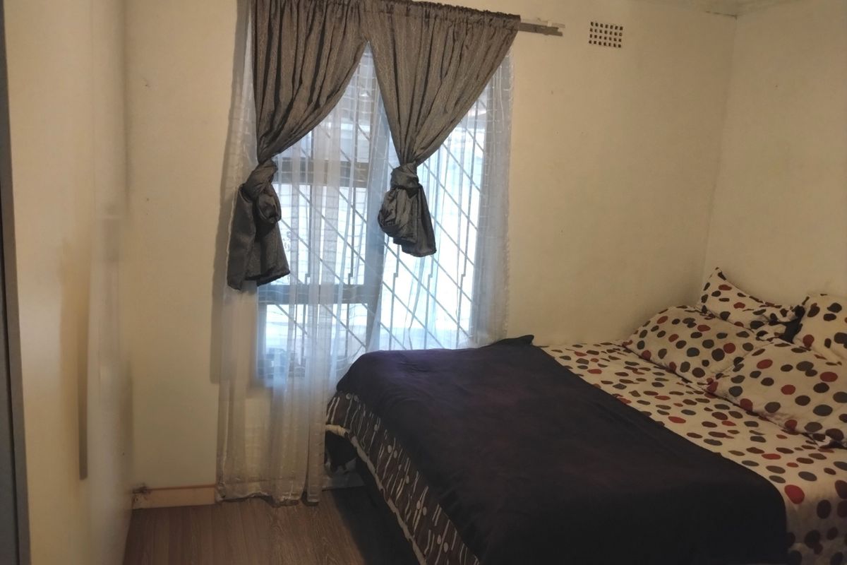 A bedroom featuring laminate flooring, a window with security bars, and a ventilation vent.