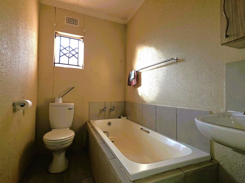 A functional bathroom featuring a standard bathtub, toilet, and wall-mounted basin, requiring cosmetic updates to modernize the space.