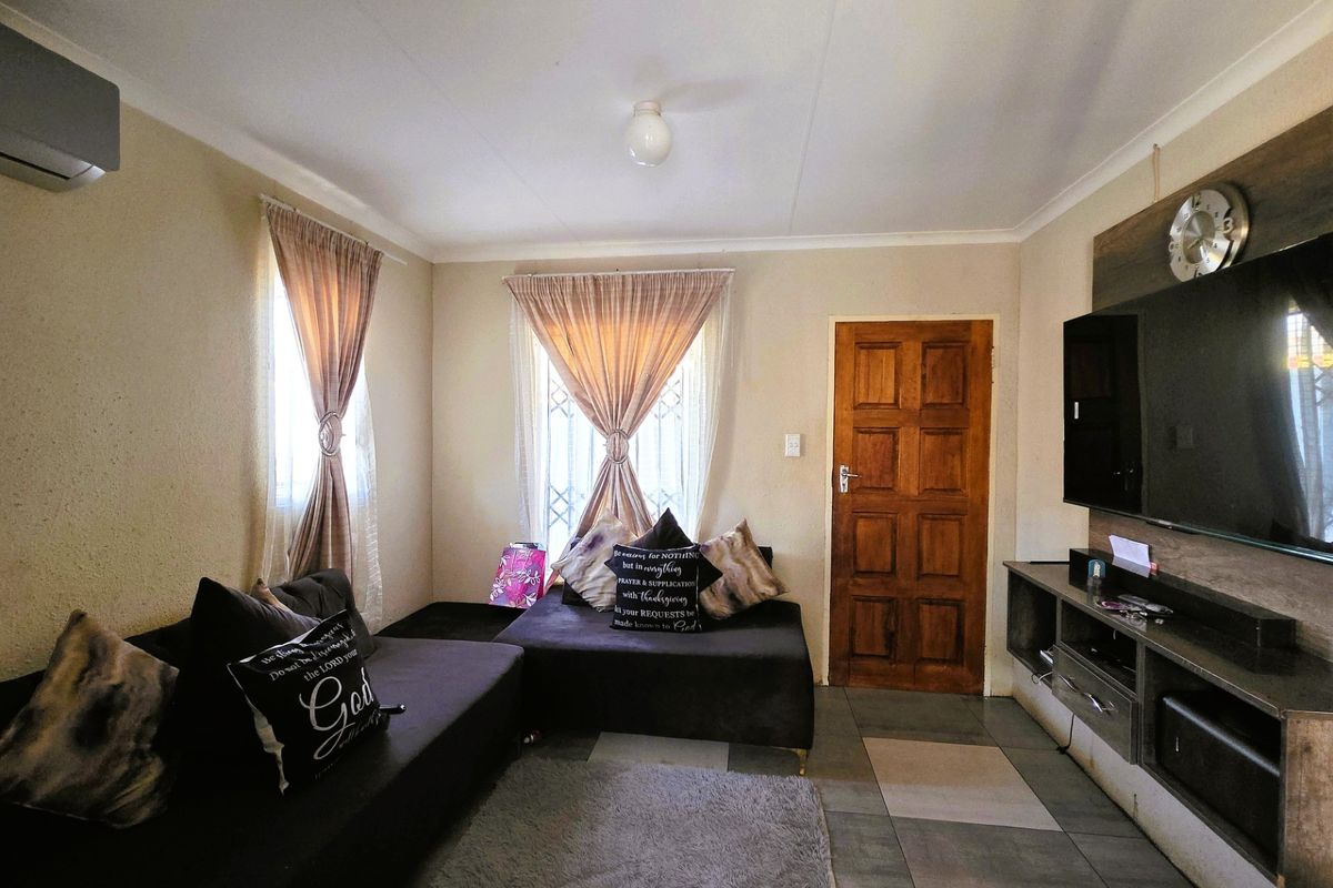A living room featuring tiled flooring, an air conditioning unit, and security bars on the windows, providing a functional and comfortable living space.