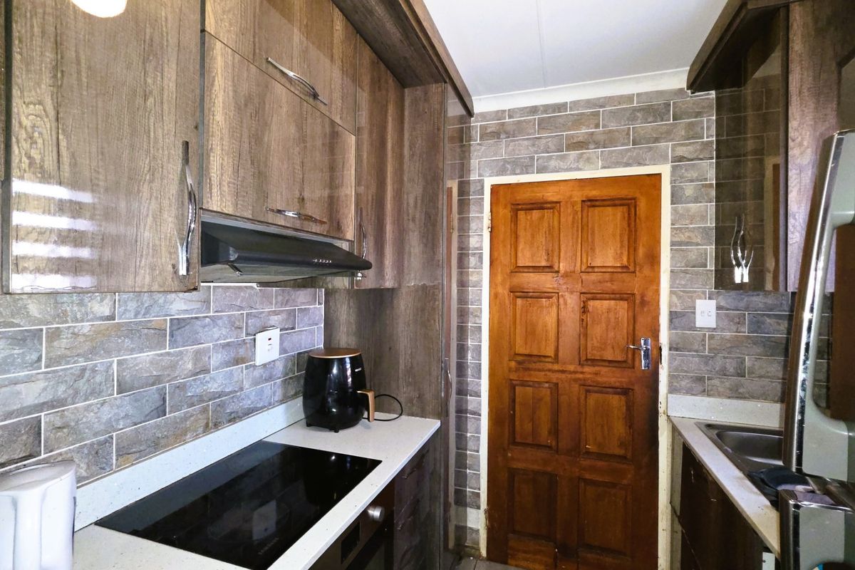 A functional kitchen featuring wood-grain cabinetry, stone-look tile backsplash, integrated electric hob, oven, and a solid timber door.