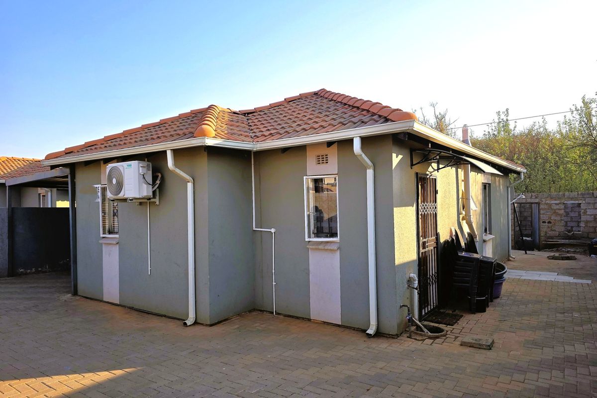 Rear view of the house featuring a tiled roof, paved exterior area, and wall-mounted air conditioning unit.