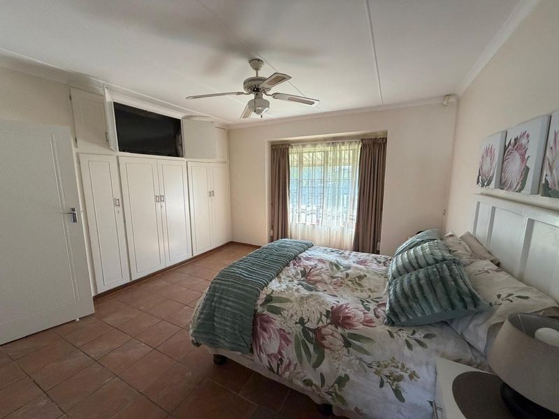 Spacious bedroom featuring built-in cupboards, a ceiling fan, and tiled flooring, offering a functional layout with natural light through the window.