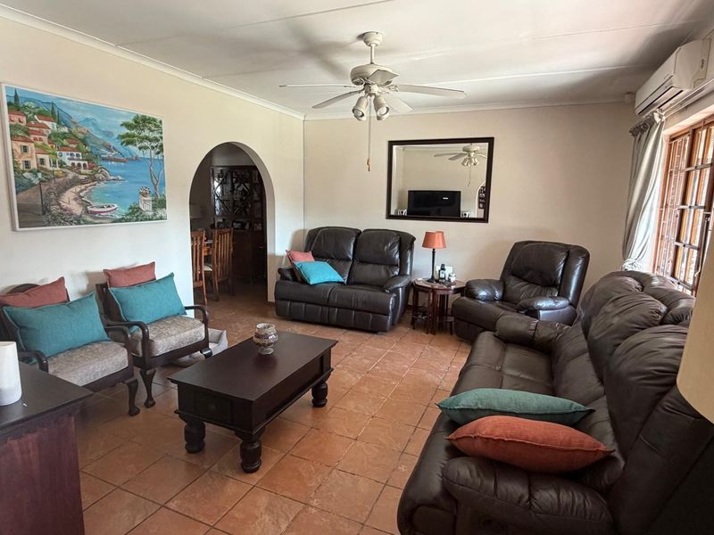 Spacious living room featuring terracotta floor tiles, a ceiling fan, and a split-system air conditioner, with an arched transition to the adjacent dining area.