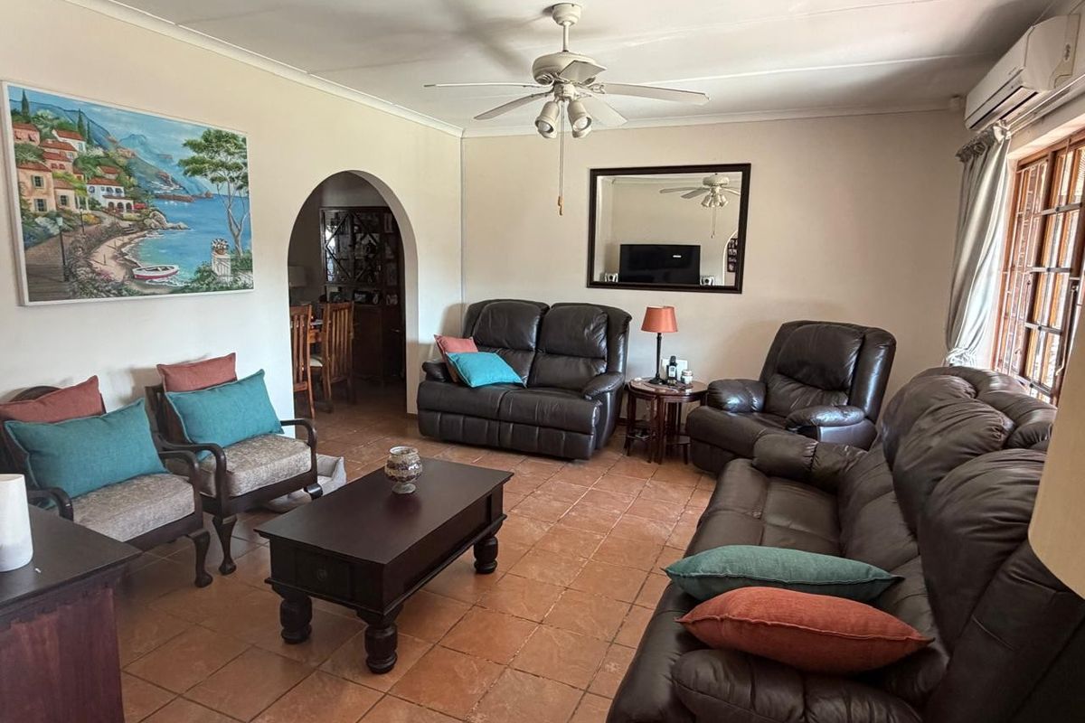Spacious living room featuring terracotta floor tiles, a ceiling fan, and a split-system air conditioner, with an arched transition to the adjacent dining area.
