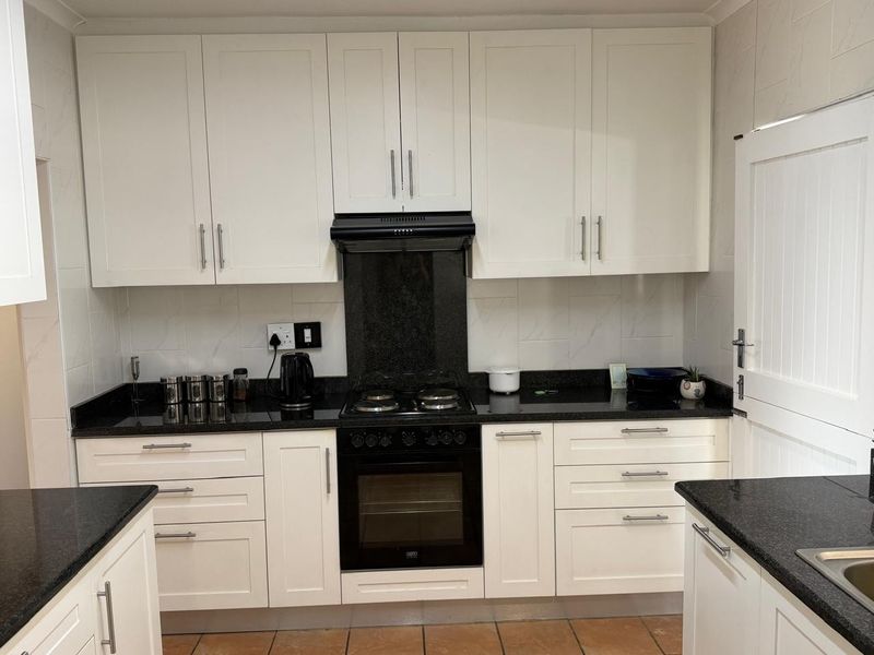 A well-maintained kitchen featuring white cabinetry, contrasting black granite countertops, a built-in oven, hob, and extractor fan with tiled backsplash.