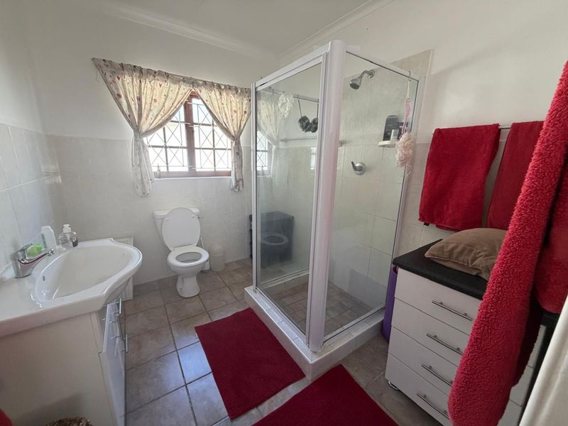A functional bathroom featuring a shower enclosure, toilet, and vanity basin with tiled finishes and a leaded glass window.