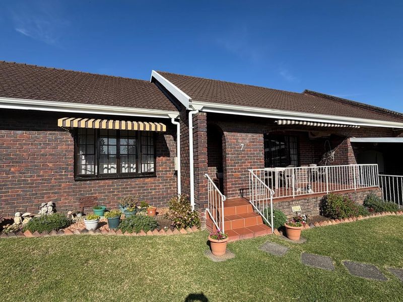 Front elevation of a face brick townhouse featuring a covered porch, tiled steps, metal railings, and classic window awnings.