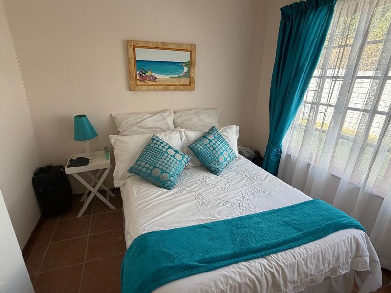 A compact bedroom featuring tiled flooring and a window with security bars, providing a functional and well-lit sleeping space.