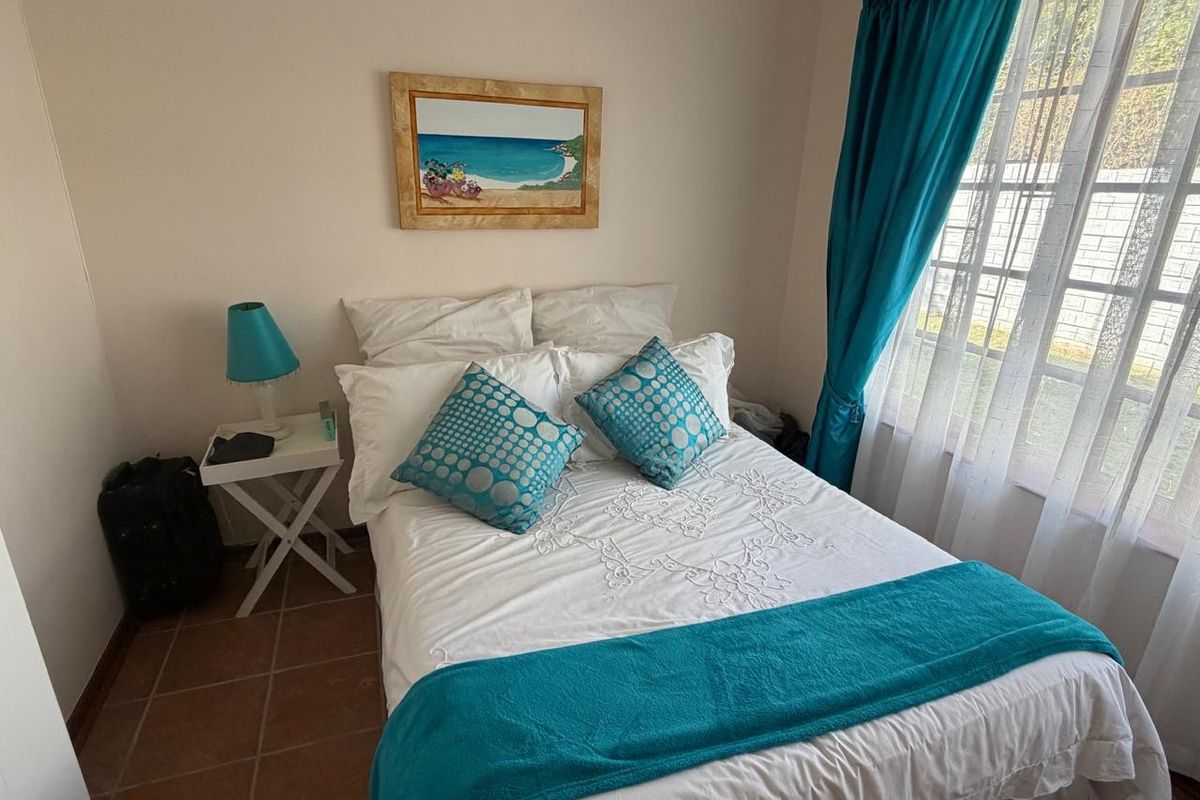 A compact bedroom featuring tiled flooring and a window with security bars, providing a functional and well-lit sleeping space.