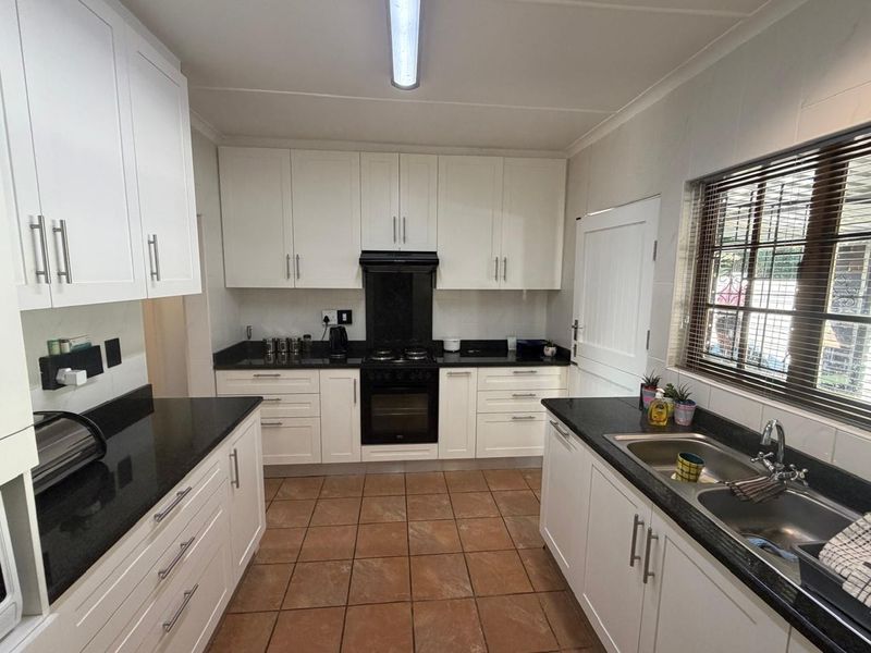 A well-maintained kitchen featuring white cabinetry, contrasting black granite countertops, a built-in oven with gas hob, and a double basin sink.