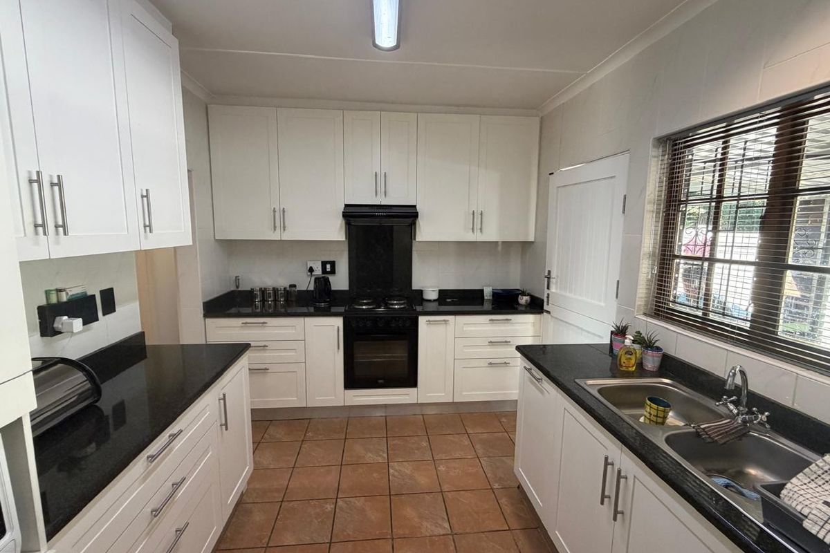 A well-maintained kitchen featuring white cabinetry, contrasting black granite countertops, a built-in oven with gas hob, and a double basin sink.