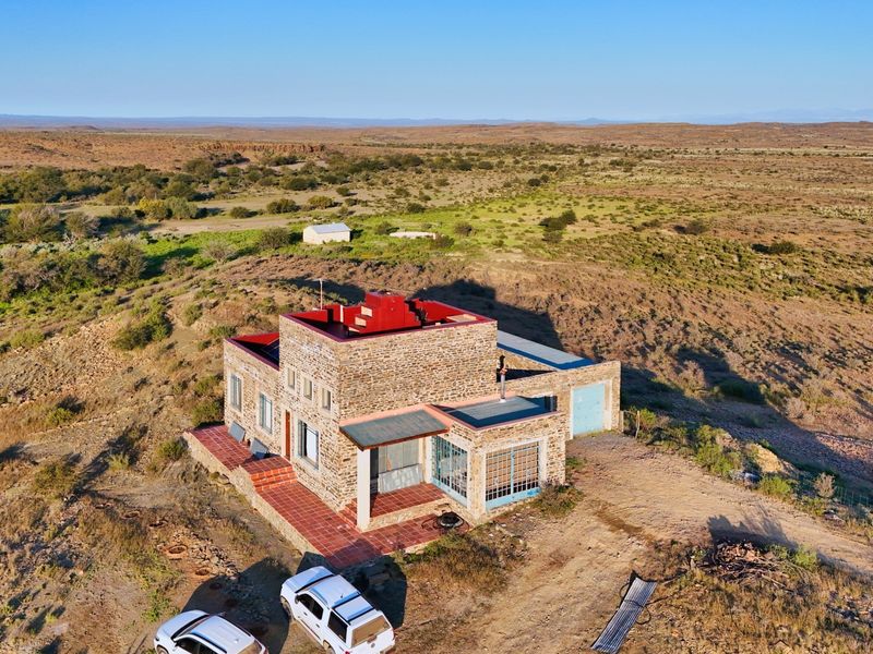 Aerial view of a stone-clad farmhouse situated in a vast rural landscape, featuring a tiled patio and integrated garage.