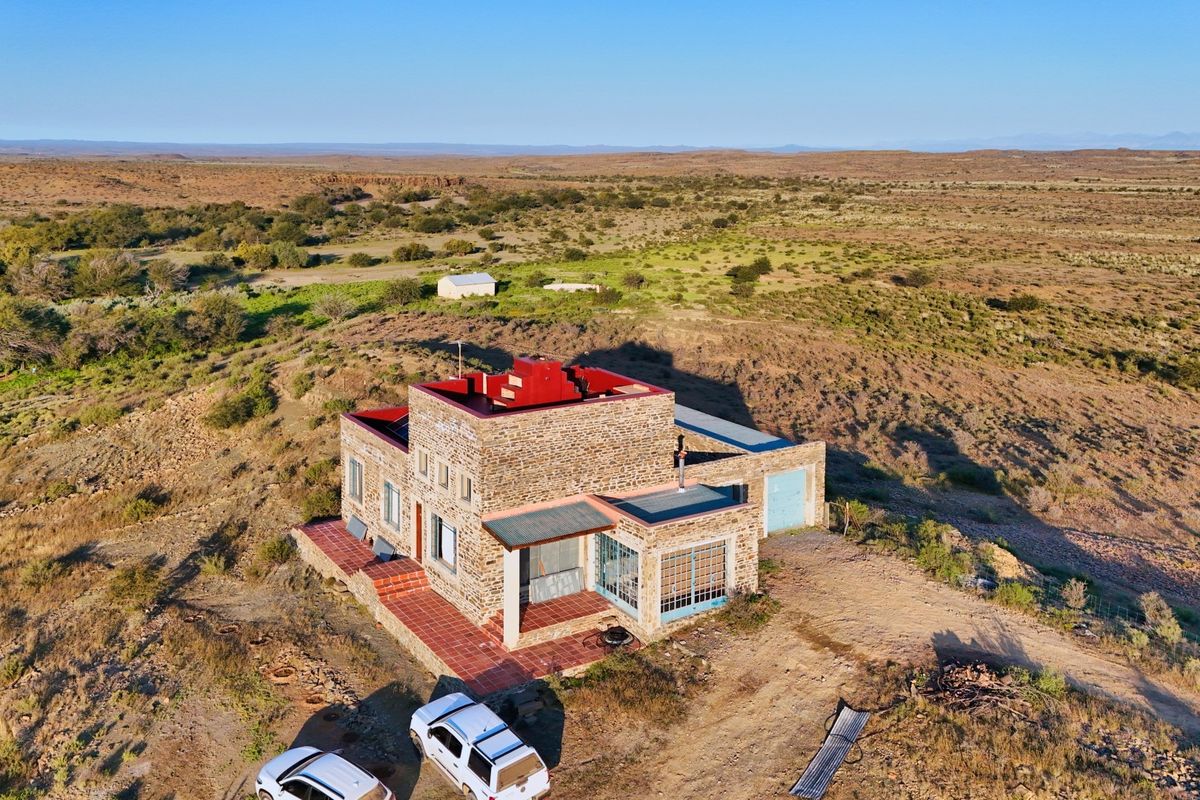 Aerial view of a stone-clad farmhouse situated in a vast rural landscape, featuring a tiled patio and integrated garage.