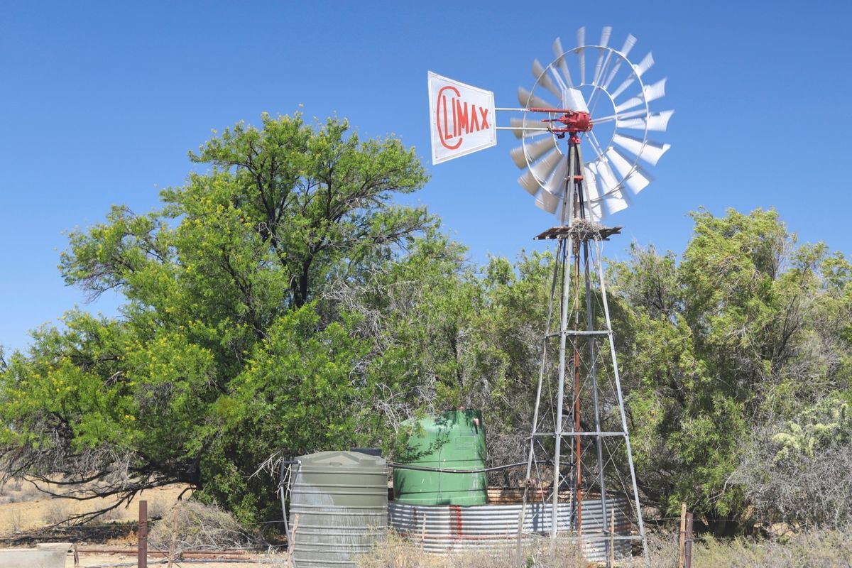 A traditional farm windmill with a Climax vane, accompanied by water storage tanks and a corrugated metal reservoir in a rural landscape.