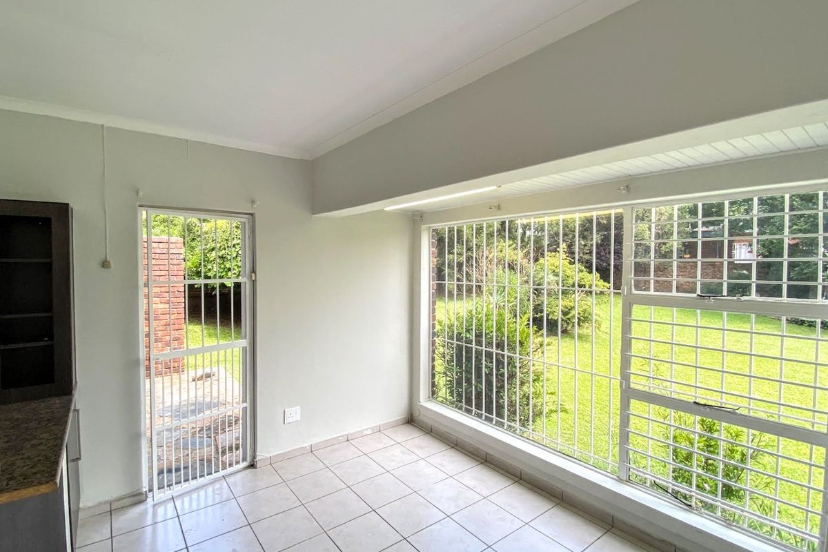 A bright, empty living area featuring large windows with security bars, tiled flooring, and direct access to the rear garden.