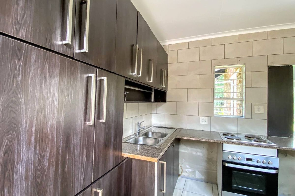 A functional kitchen featuring dark wood-look cabinetry, granite-style countertops, a stainless steel sink, and a built-in electric oven and hob.