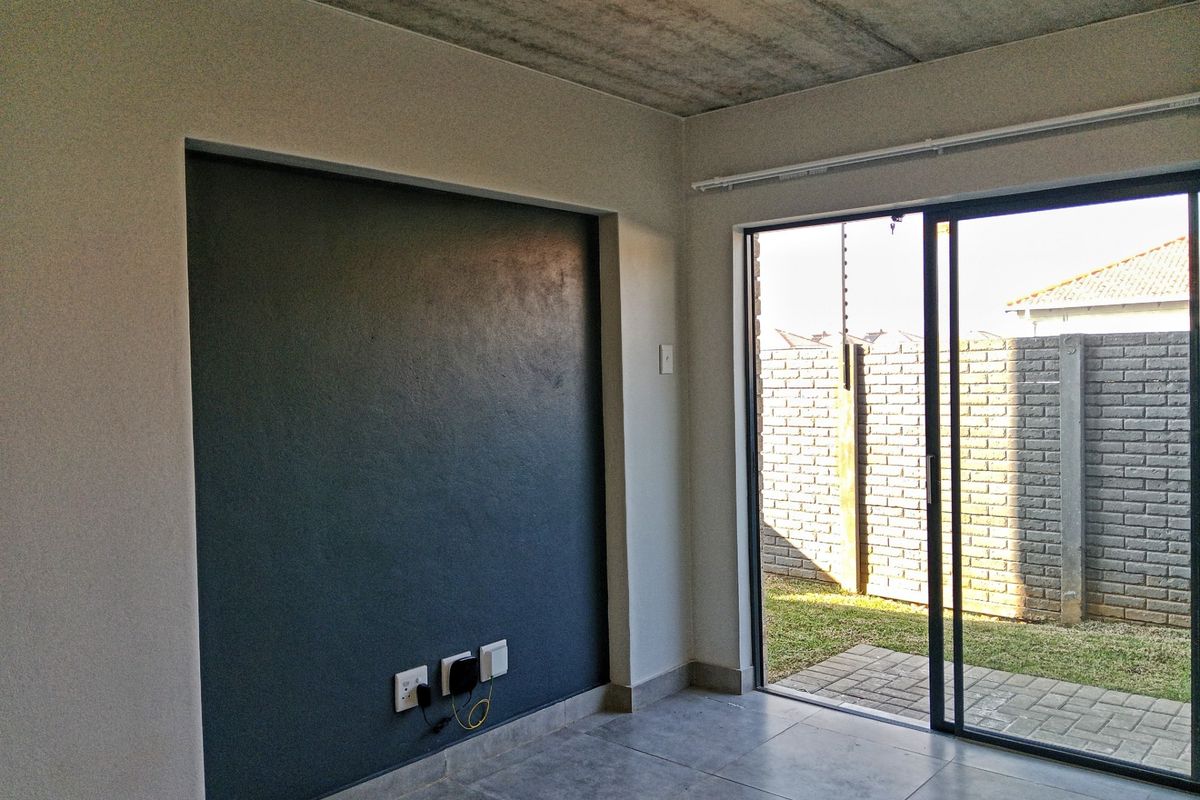 A modern living area featuring a dark accent wall, exposed concrete ceiling, tiled flooring, and sliding glass doors leading to a private outdoor space.